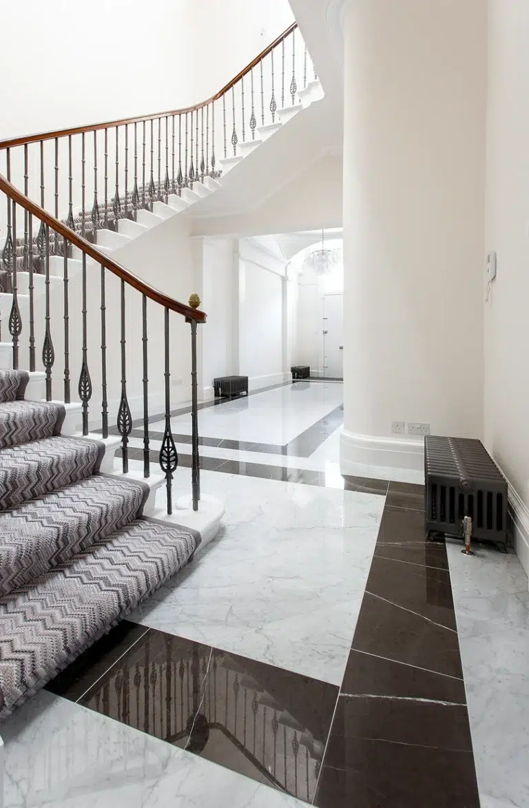 Marble hallway floor with black borders at the foot of a staircase by Stonecraft